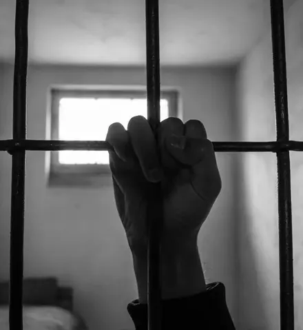 A person 's hand is seen through bars of a jail cell.